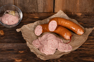 Auf dem Bild ist unsere Bio Land.Luft Regensburger Wurst zu sehen, angerichtet auf Backpapier, daneben eine kleine Schale Wurstsalat